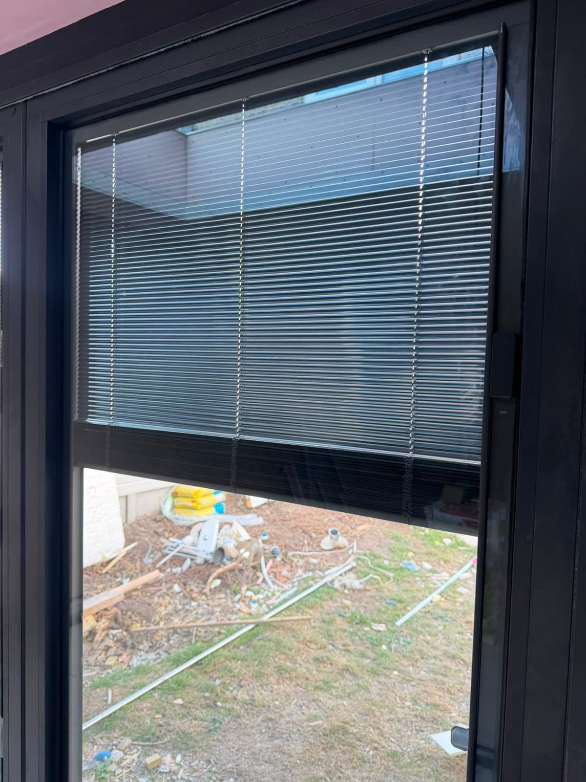 An integral blind half raised inside an anthracite aluminium window, showing the blind sitting within the glass