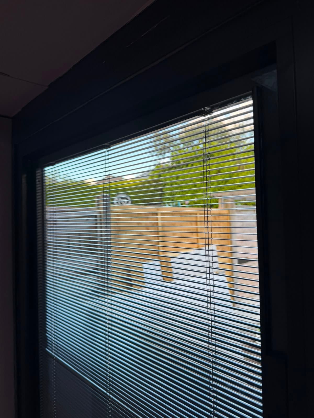 An anthracite aluminium window with an integral blind, looking out onto a garden