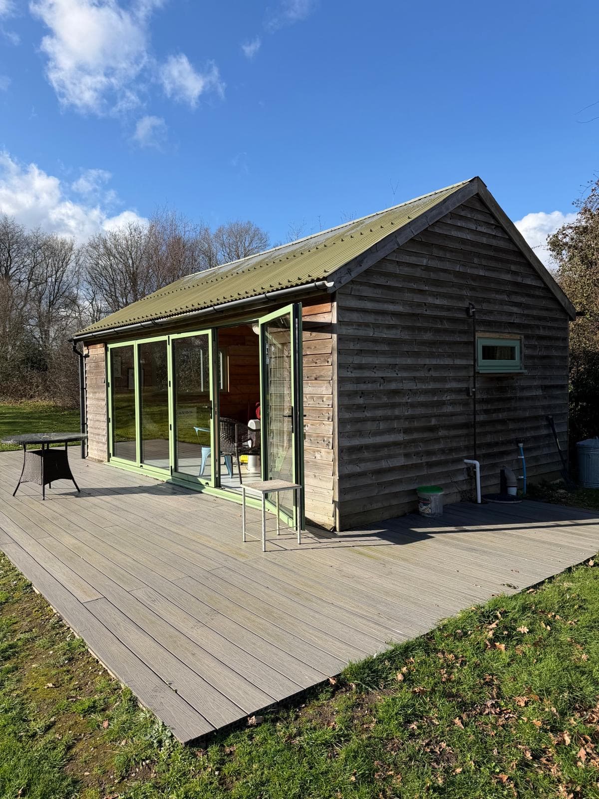 A sage-green aluminium bi-fold door fully open on a timber-clad garden room, a real Wilshaw installation