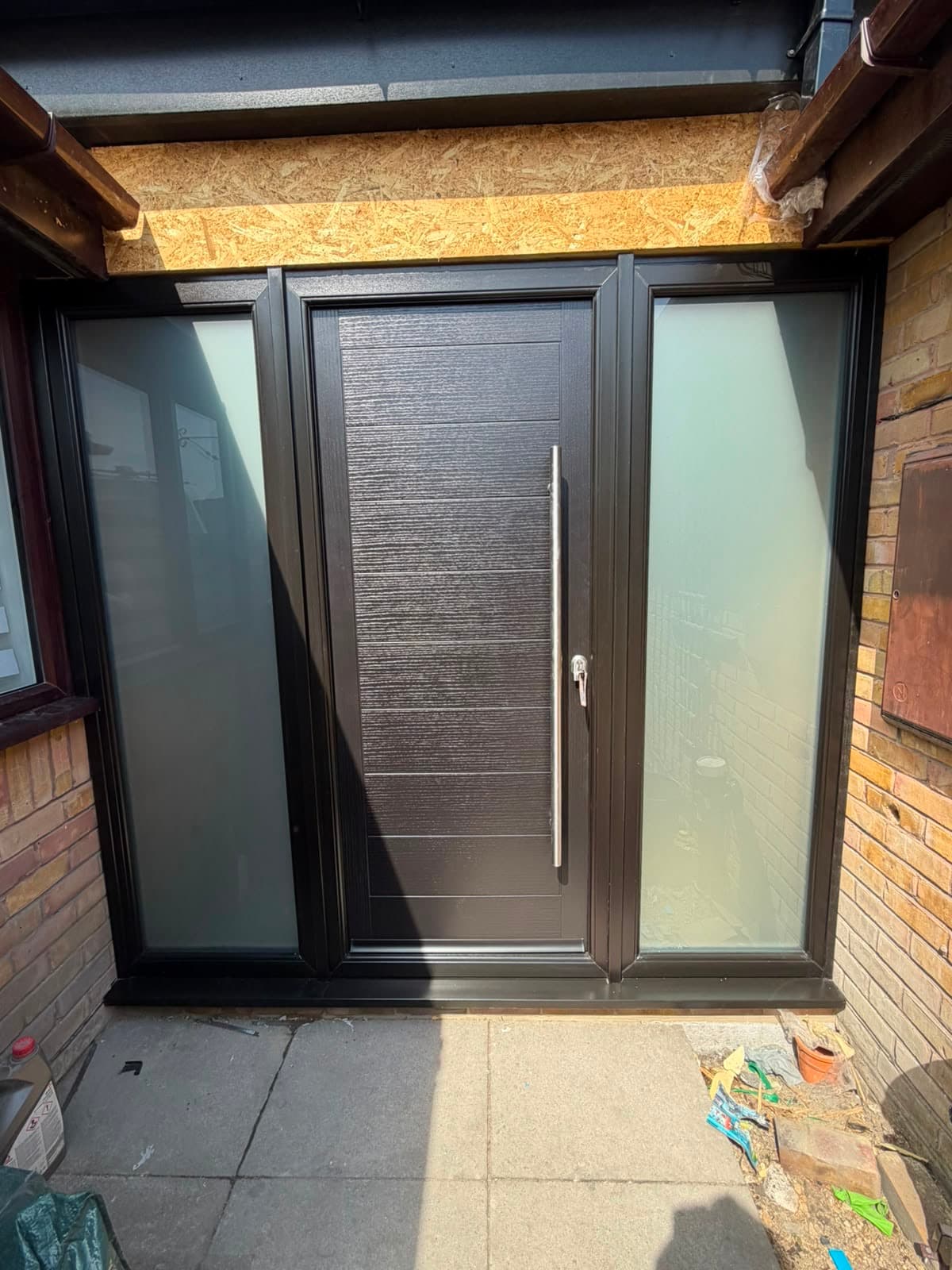 An anthracite composite front door with a long bar handle and plain glazed sidelights, a real Wilshaw installation