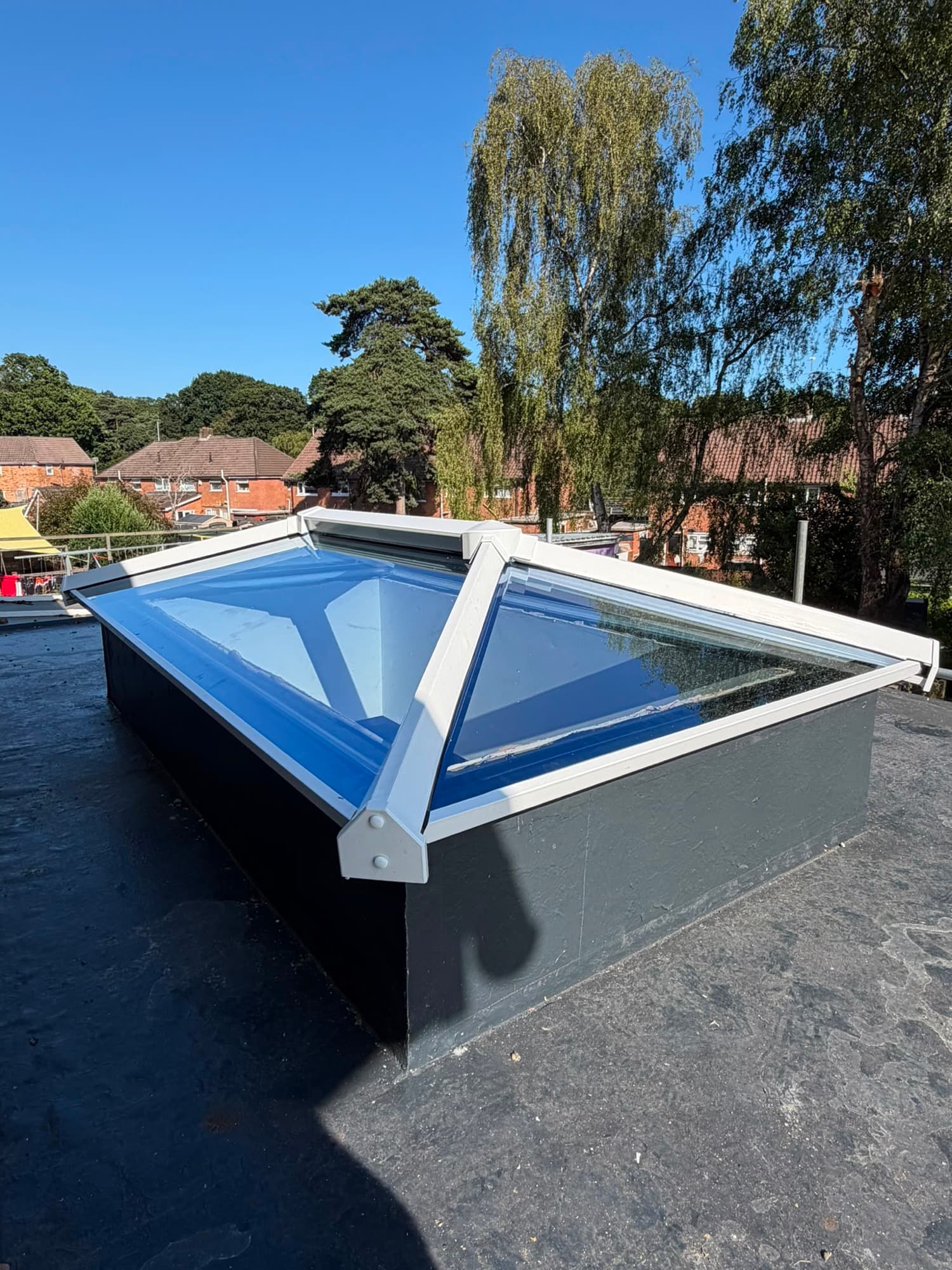 A white-framed pyramid roof lantern with a central ridge bar, fitted on a flat felt roof upstand