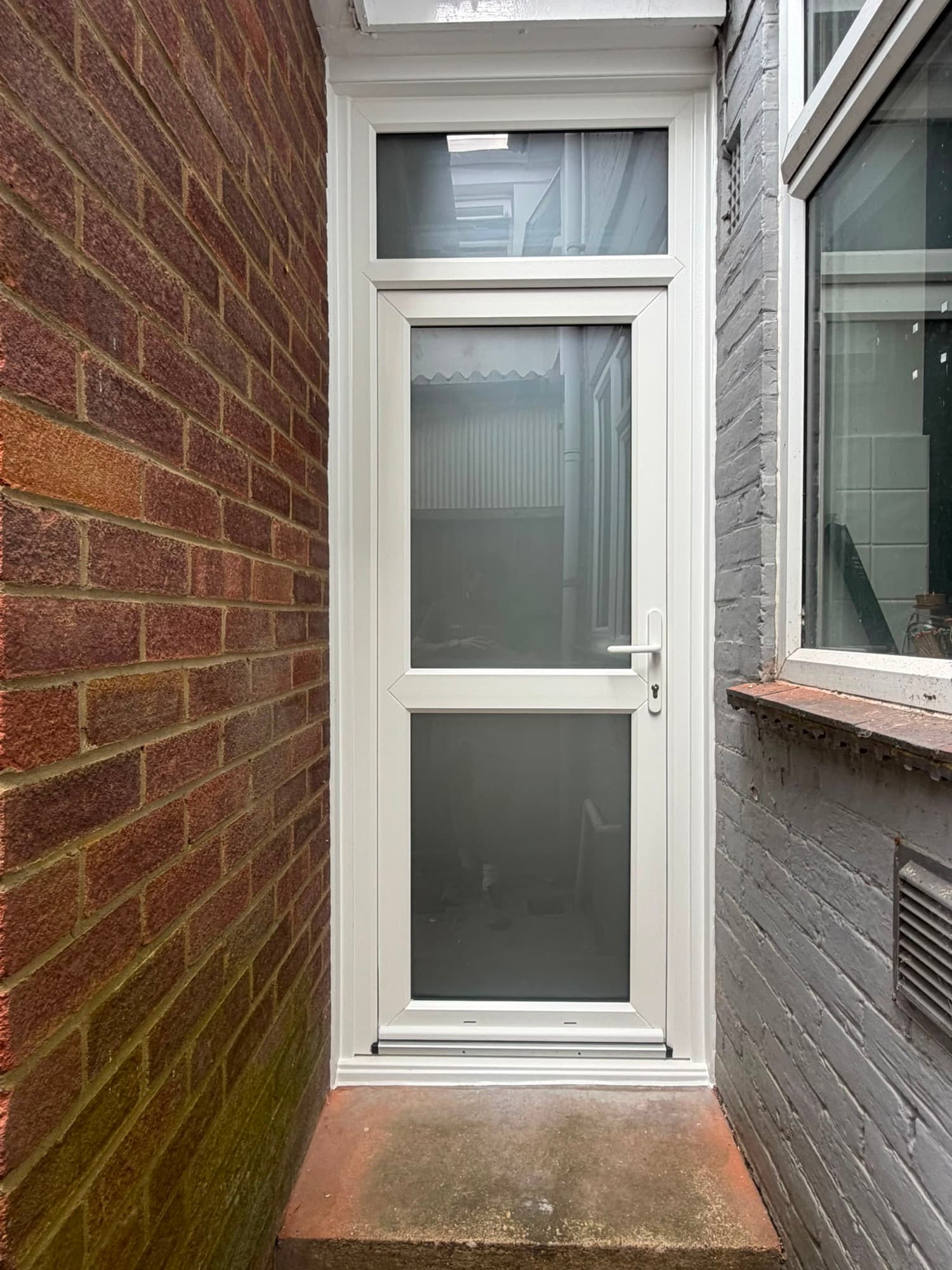 A white uPVC part-glazed door fitted in a narrow brick side passage, a real Wilshaw installation