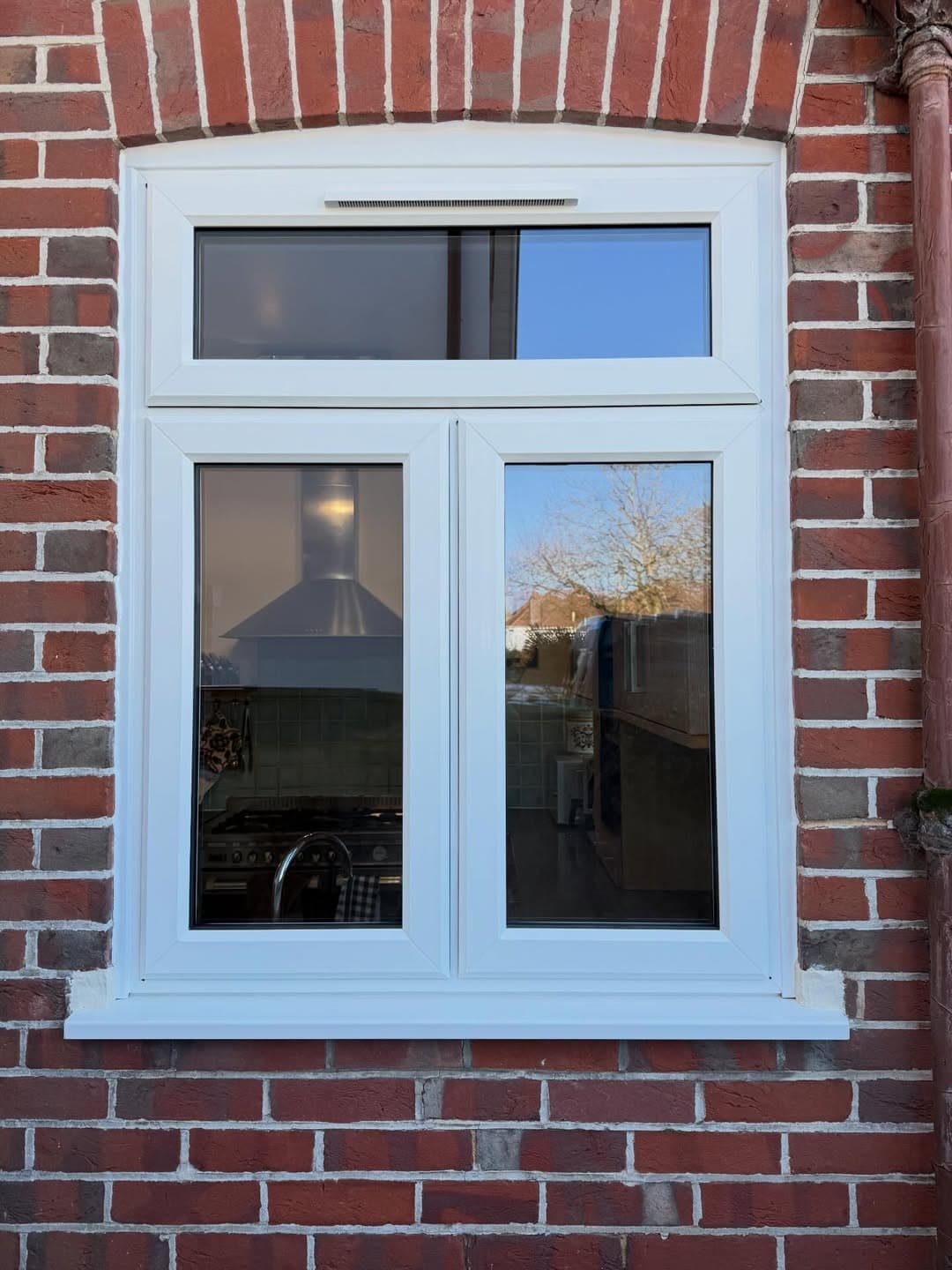 A white uPVC casement window under a brick arch in a period elevation, fitted by Wilshaw Glazing