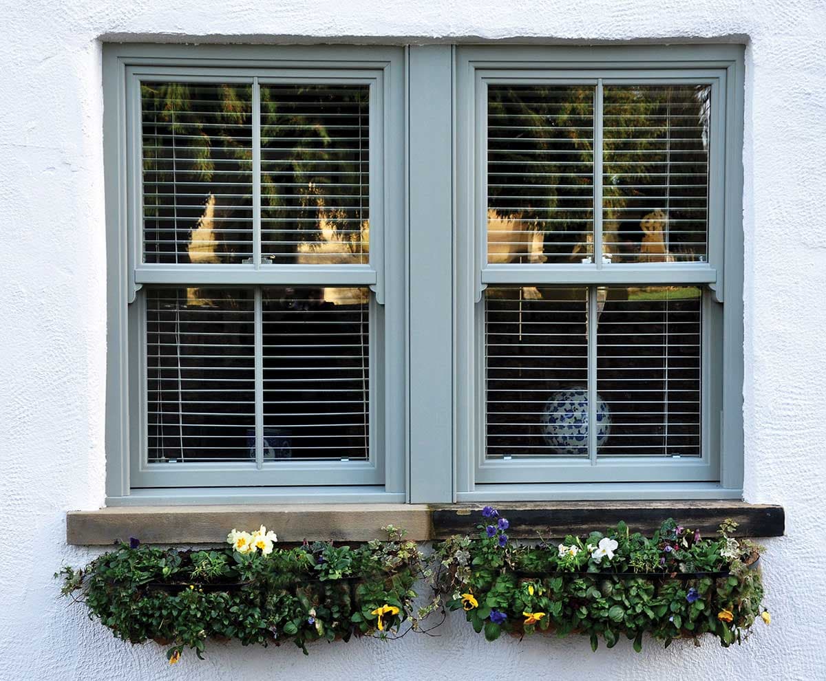 A sage green uPVC sash window in a cottage elevation, matching a traditional profile
